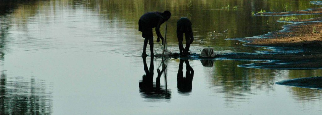 Two people examine a fishing net in the shallows of a river